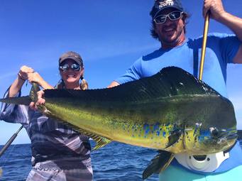 A man and woman holding sidewise a large colorful Mahi on board the fishing boat on a clear day
